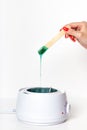 Vertical shot of woman hand holding wooden depilatory spatula, dripping green hot wax into thermostat heater