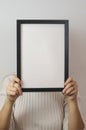 Vertical shot of a woman holding a plain white blank sign paper with a black frame covering her face Royalty Free Stock Photo