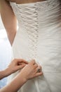 Vertical shot of a woman making a bow-knot on the back of the bride& x27;s wedding dress. Royalty Free Stock Photo