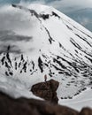 Vertical shot of a woman on a rocky cliff with a snow-peaked mountain background