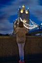 Vertical shot of a woman standing at the illuminated Tower Bridge at night Royalty Free Stock Photo