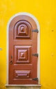 Vertical shot of a wooden door with a white frame on a yellow wall Royalty Free Stock Photo