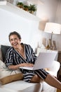 Vertical shot of a 50-year-old cancer overcomer sitting on the sofa with a laptop Royalty Free Stock Photo