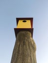 Vertical shot of yellow and red bird house on a wooden pole against atmospheric blue sky Royalty Free Stock Photo