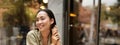 Vertical shot of young asian woman working on remote from outdoor cafe, sitting with laptop and smiling, studying Royalty Free Stock Photo