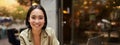 Vertical shot of young asian woman working on remote from outdoor cafe, sitting with laptop and smiling, studying Royalty Free Stock Photo