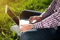 Vertical shot Young Caucasian man sitting under a tree, typing on a laptop Royalty Free Stock Photo