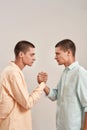 Vertical shot of young caucasian twin brothers looking at each other, holding hands while standing face to face isolated Royalty Free Stock Photo