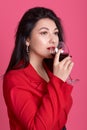 Vertical shot of young celebrating beautiful Caucasian woman wearing red elegant dress holding wine glass, enjoying its taste, Royalty Free Stock Photo