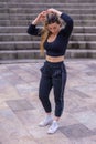 Vertical shot of a young female adult wearing a black tank top and jogging pants fixing her hair