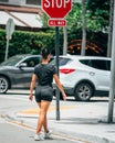 Vertical shot of a young female in athleisure crossing a road near a stop sign