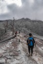 Vertical shot of a young female hikers walking below a burnt forest trunk around the Volcanic cone in the danger zone in the