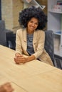 Vertical shot of a young happy mixed race woman, female office worker sitting at desk in the modern office and smiling Royalty Free Stock Photo