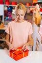 Vertical shot of young sales woman holding and using golden ribbon to tie bow for red wrapped gift box for Christmas Royalty Free Stock Photo