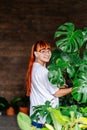 Happy woman gardener wearing yellow overalls, holding a young plant Philodendron in plastic pot. Home gardening, love of