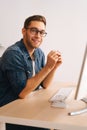 Vertical side view shot of smiling handsome young freelance designer male in stylish glasses working on desktop computer Royalty Free Stock Photo