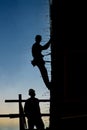 Vertical silhouette of a construction worker in harness on the side of a buiilding under construction