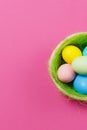 Vertical six colorful pastel painted Easter eggs in basket with green grass isolated on pink background. Happy Easter