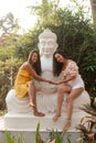 Smiling barefoot long haired woman in open clothes sit on white plaster statue of Buddha, look at camera and hold hands Royalty Free Stock Photo