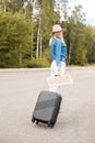 Vertical smiling blond woman hitchhiker with carton plate anywhere carrying roll aboard suitcase and waiting car stop