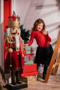 Vertical smiling, playful, artistic curly girl standing near big Nutcracker toy in crown, near present boxes in toy shop Royalty Free Stock Photo