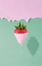 Vertical of a strawberry dripping with pink paint on a pink and green background.