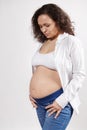 Attractive ethnic pregnant woman posing bare belly, isolated over white background. Pregnancy fashion. Body positivity