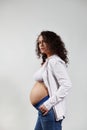 Vertical portrait of curly haired pregnant woman, posing bare belly on isolated white backdrop. Happy pregnancy 6 month