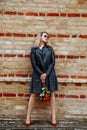 Vertical of stylish, confident blond woman with make-up and in sunglasses, black leather jacket against wall with roses Royalty Free Stock Photo