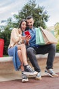 Vertical. Surprised couple using a cellphone to find sales, shopping online sitting with bags. Man and woman having fun Royalty Free Stock Photo