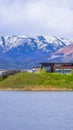 Vertical tall Buildings and snowy mountain beyond the grassy shore of a lake on a cloudy day