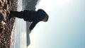 Vertical of Toddler throwing pebble in sea on stony coast