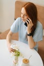Vertical top view of happy young woman holding cup with hot coffee in hands talking on mobile phone sitting at desk in Royalty Free Stock Photo
