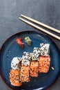 Vertical top view of a pair of chopsticks over a plate of gourmet sushi rolls