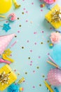 Vertical top view of table set with sweets, wrapped gifts, party hats, noise-maker, candles, straws, balloons blue backdrop