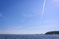 Vertical trail from the plane against the blue sky with cirrus clouds above the water surface of the lake