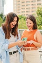 Vertical. Two cheerful smiling women watching and showing sale, news and social media on their smartphone app outside at Royalty Free Stock Photo