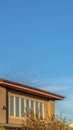 Vertical Upper storey of a home with brown wall lined with windows against vast blue sky