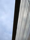 vertical upwards view of a modem office building with a blue cloudy sky on one side reflected in the window