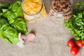 Various types of pasta, fusilli and farfalle, in glass jars next to tomato and garlic and basil