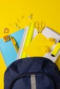 Vertical video of composition with backpack and school items on yellow surface