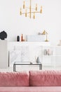 Vertical view of backside of powder pink sofa in white modern living room interior with coffee table, golden chandelier and maps Royalty Free Stock Photo