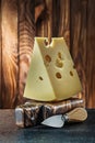 Vertical view big piece of milk maasdam cheese on little cutting board and knife old wooden background