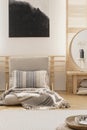 Vertical view of black and white abstract painting above white warm blanket and patterned pillow on beige futon in elegant natural