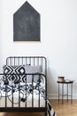 Blackboard on the wall of teenagers bedroom with black and white patterned bedding on single metal bed, real