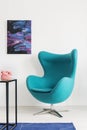 Vertical view of blue egg chair next to metal shelf with pink telephone, cosmos graphic on the wall, real photo with copy space Royalty Free Stock Photo