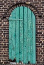 Vertical view of a broken blue-colored wooden door at the entrance of a brick-built building