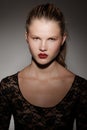 Close up frontal portrait of a beautiful blonde girl with hair gathered in a ponytail, red lips, on dark background.