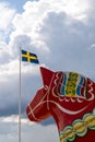 Vertical view of a colorful Swedish Dala horse and the Swedish flag under an expressive sky