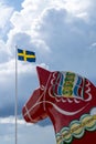 Vertical view of a colorful Swedish Dala horse and the Swedish flag under an expressive sky